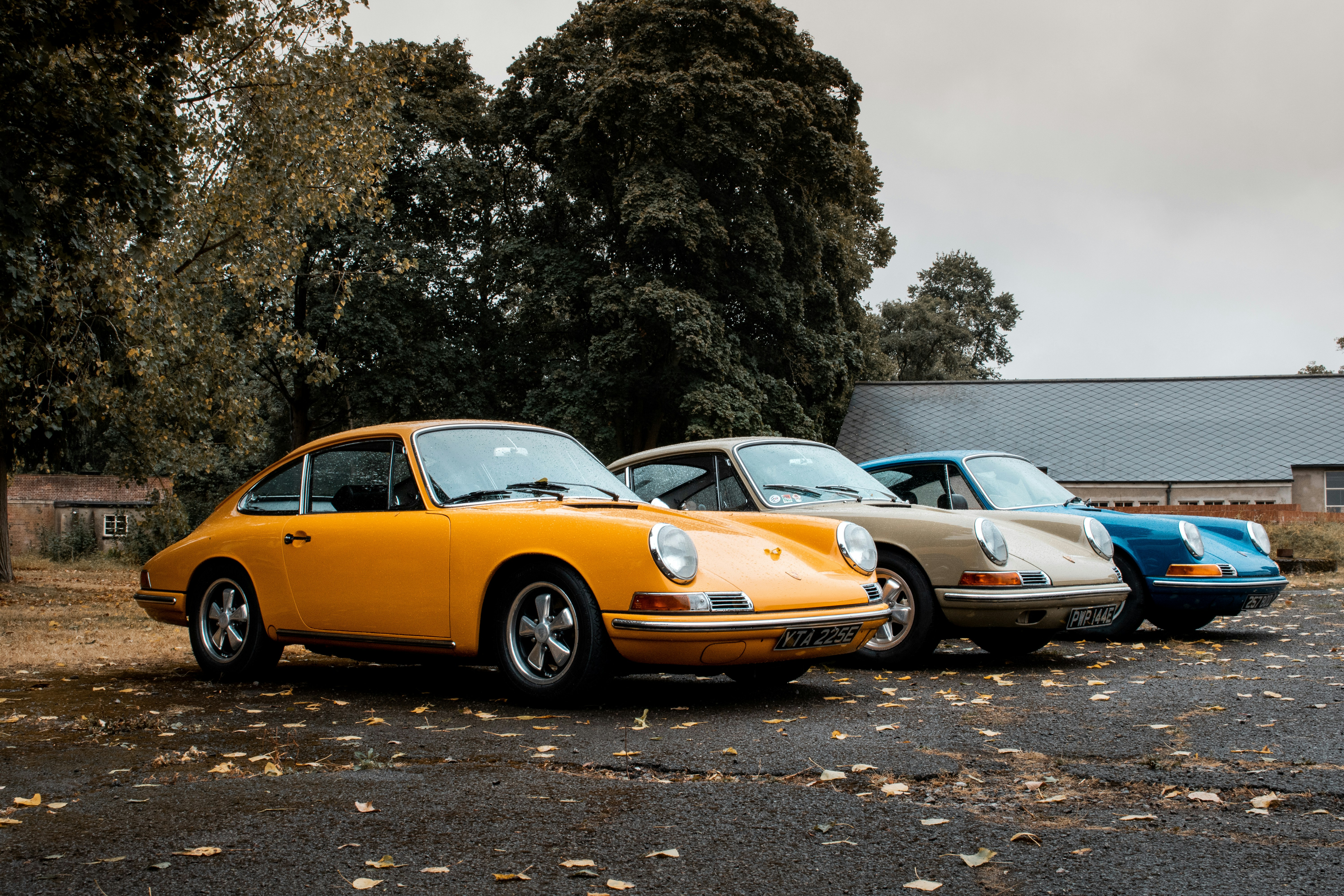 Three classic Porsche 911s parked outside a brick workshop